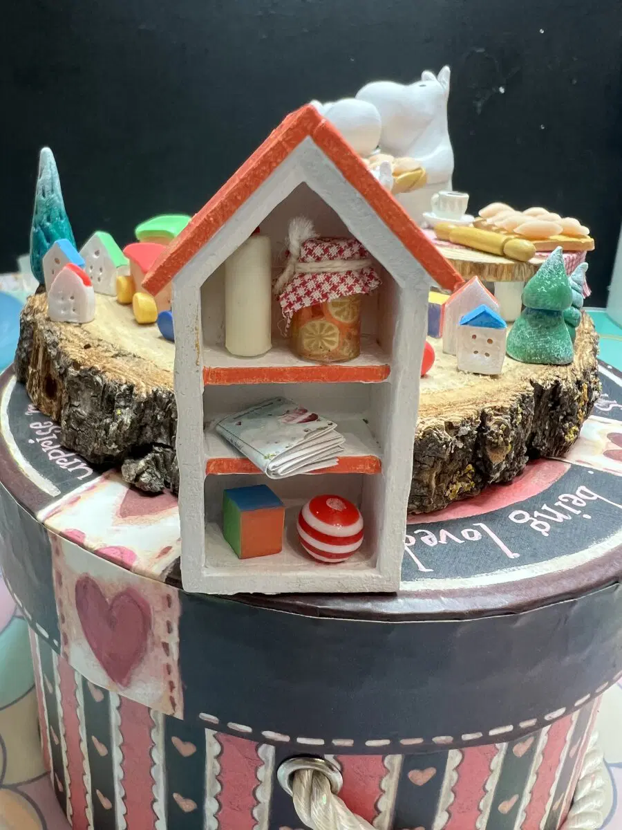 Шкафчик, в углу свечка, баночка апельсинового джема, тетрадь, кубик и мяч.