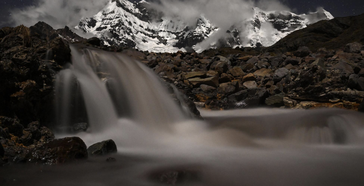 NEVADO AUZANGATE, ПЕРУ / Окаймляемый облаками на фоне ночного неба, снежная Nevado Auzangate, самая высокая гора в Андах на юге Перу, возвышается над водопадом. Ледниковое таяние является основным источником пресной воды для экосистем ниже по течению.